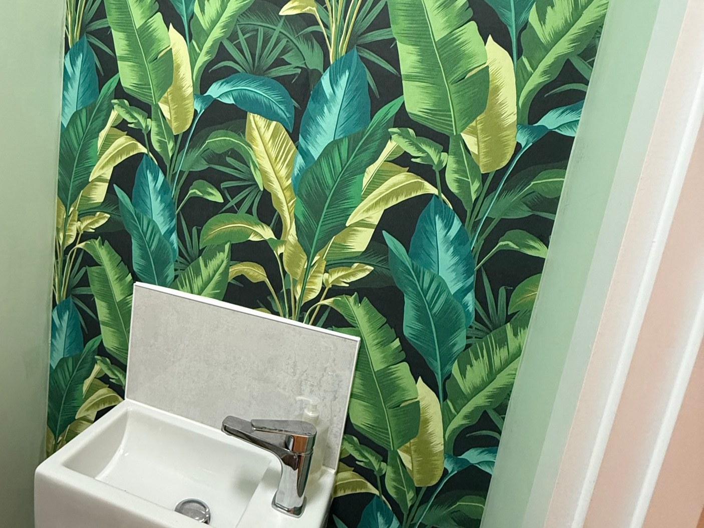 Downstairs cloakroom with bold tropical banana-leaf feature wallpaper and a compact wall-hung basin fitted by Final Touch in Aylesbury
